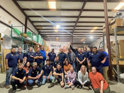 Team members wearing navy blue Southern Air uniforms posing together in warehouse with Happy Fall banner in background.