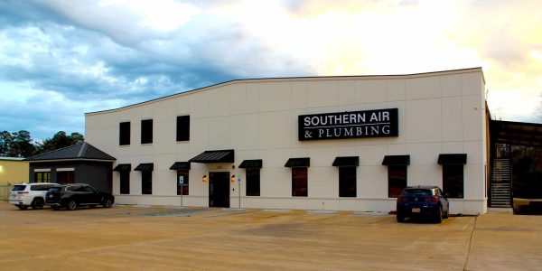 Modern commercial building with cream-colored exterior, black awnings, and Southern Air & Plumbing signage, with parked vehicles in front.